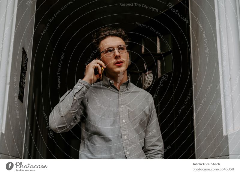 Focused young man talking on smartphone phone call conversation concentrate pensive corridor communicate device eyeglasses shirt gadget connection casual