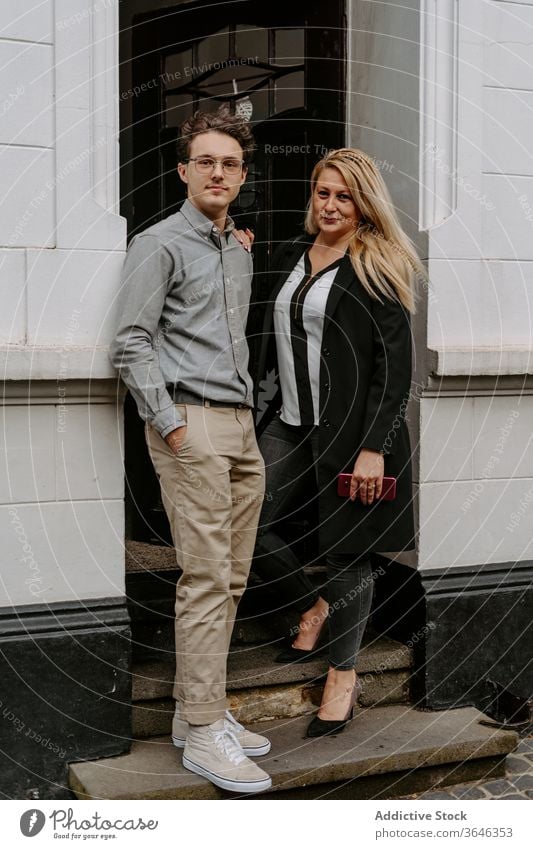 Content couple in doorway on street colleague formal modern building entrance positive content confident professional hand in pocket business break outfit