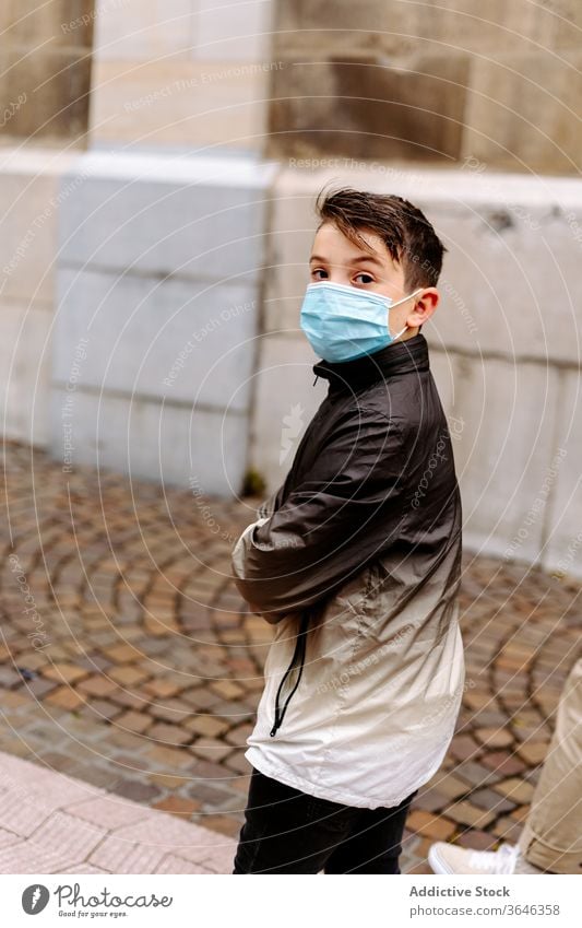 Boy wearing protective mask walking on street boy respirator sidewalk serious casual stroll coronavirus epidemic jacket arms folded outbreak childhood lifestyle