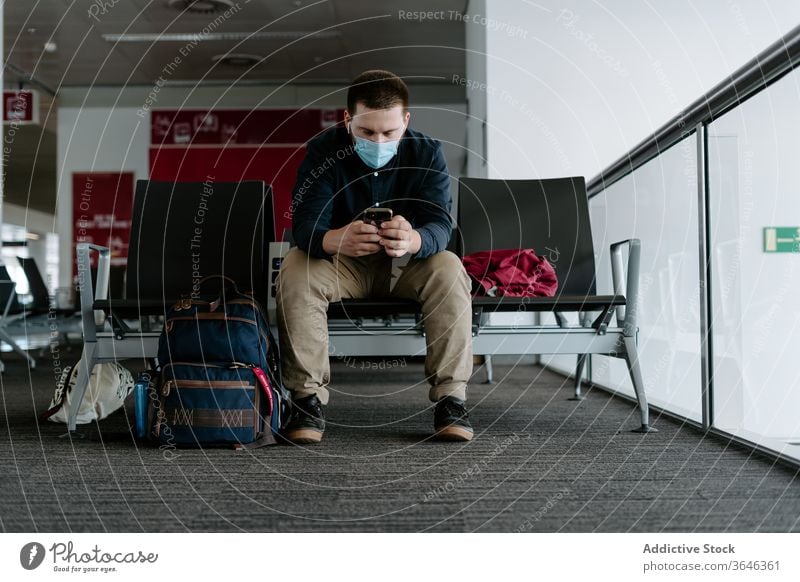 Male passenger in respirator using smartphone while waiting for flight man browsing mask airport coronavirus device travel epidemic gadget surfing covid 19
