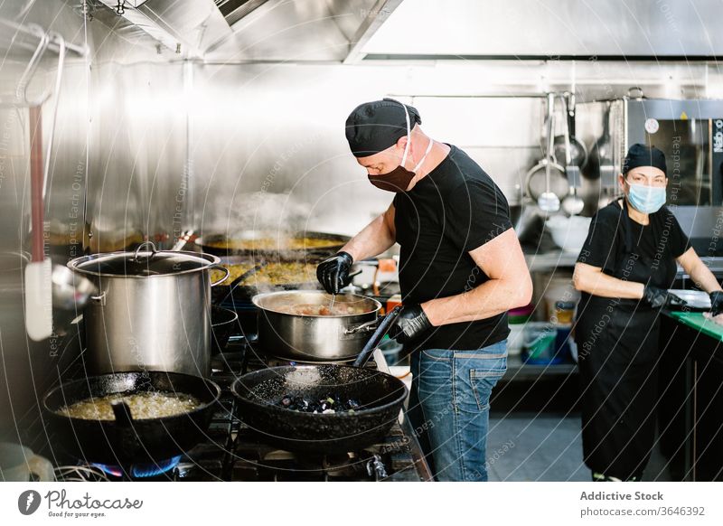 Focused male chef in face mask chef preparing meal woman respirator focus serious kitchen restaurant coronavirus ingredient food cook cooking busy glove