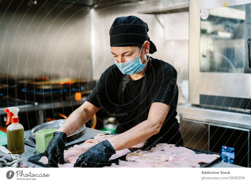 Focused female chef in face mask chef preparing meat woman respirator tray focus serious kitchen restaurant coronavirus ingredient food cook knife busy glove