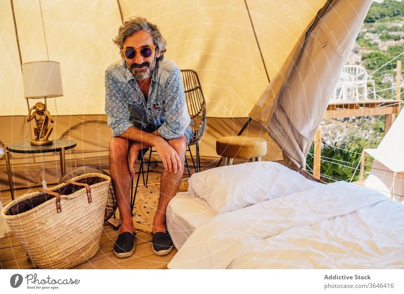 Cheerful man resting in traveling camp traveler content mature relax cozy resort creative glad comfort chair campsite summer sunglasses smile casual enjoy happy