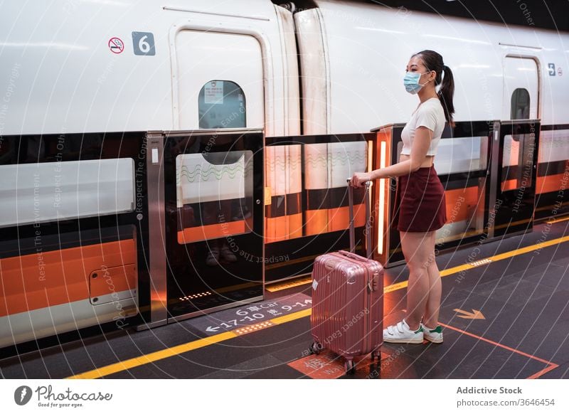 Asian woman in respirator waiting to board train in station railway station suitcase travel platform coronavirus calm cabin passenger covid 19 epidemic mask