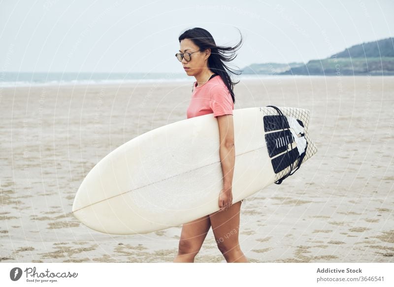 Content female surfer walking on beach with surfboard woman sandy carry content sea casual seaside carefree activity young sporty tranquil lifestyle sunglasses
