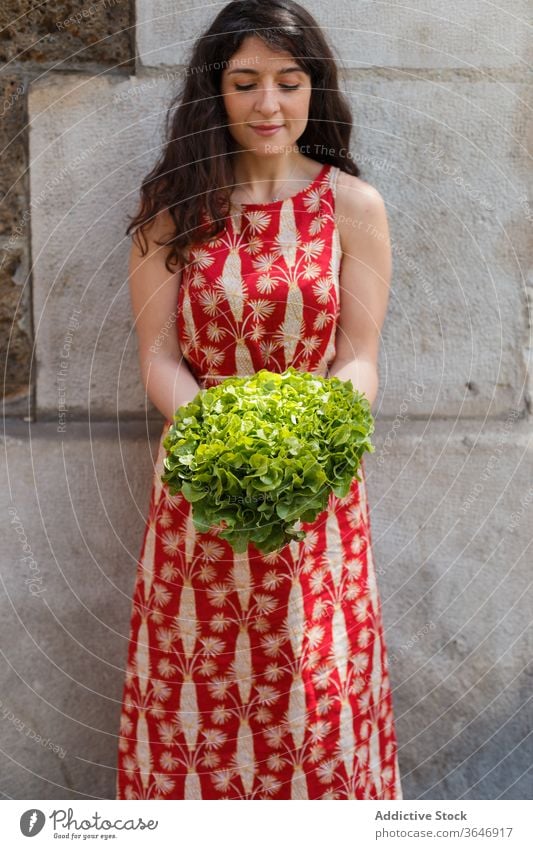 Content woman with bunch of lettuce fresh ripe green summer season organic vitamin female building tranquil stone stone wall healthy calm slim plant food