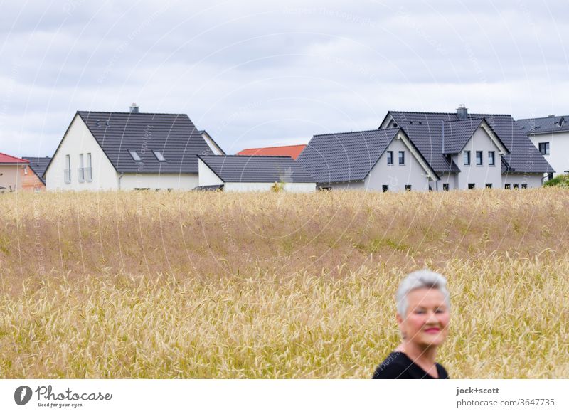 Land with densely overgrown grain fields gets a new face Woman portrait Face White-haired Smiling Forward Female senior Sky New settlement Detached house Grain