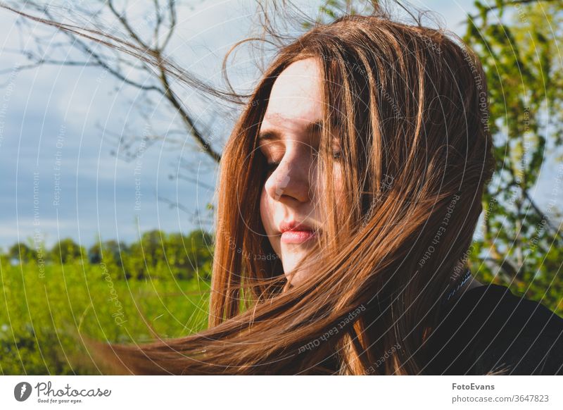 Girl is standing with blowing hair in nature, hand on head - a Royalty Free  Stock Photo from Photocase
