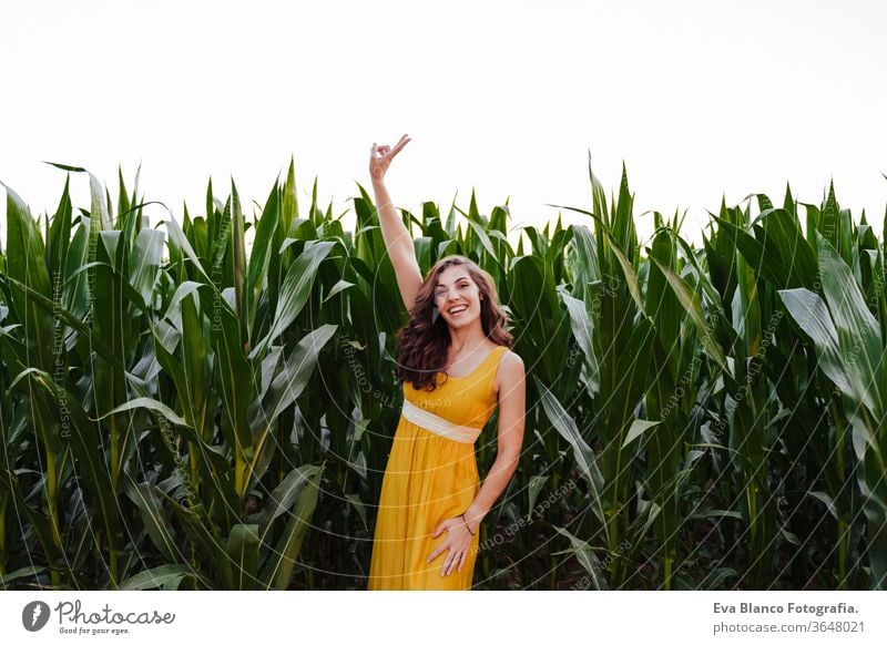 portrait of young beautiful woman wearing a yellow dress standing in a green corn field. Summertime and lifestyle 1 V sign beauty carefree casual caucasian