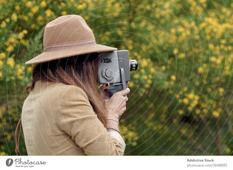 Photographer recording video with old video camera in garden photographer eyes closed bloom flower tree park branch focused stylish retro nature beauty blossom