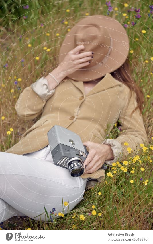 Faceless woman resting on grass with retro video camera hat elegant meadow cover face flower countryside vintage lying hide photographer lens relax garden
