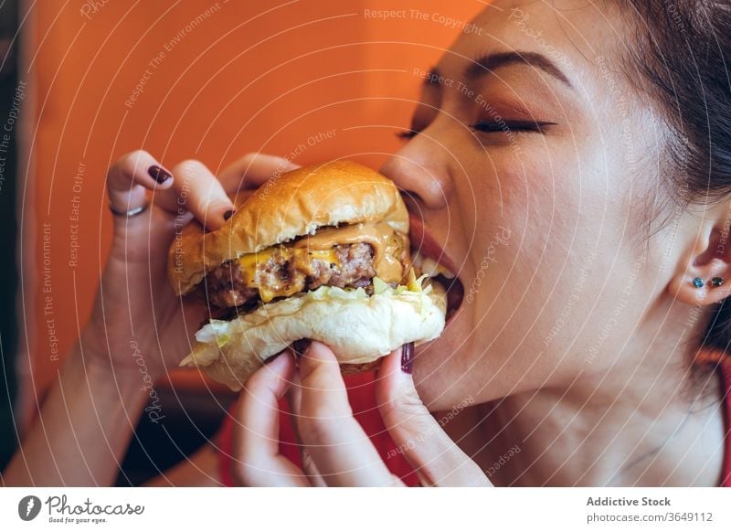 Cheerful Asian woman eating burger cafe delicious meat cutlet enjoy cheese fast food female asian ethnic sauce beef tasty meal lunch cuisine appetizing