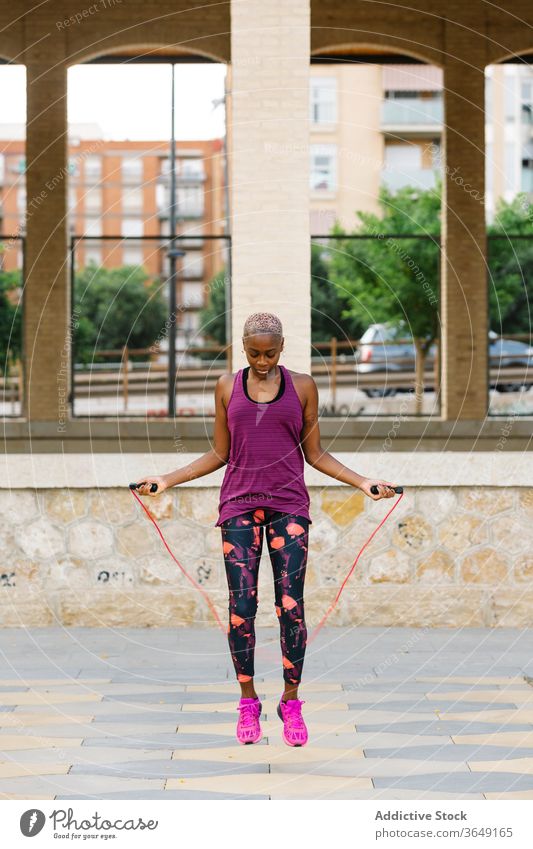 Black sportswoman jumping rope on embankment in city during workout athlete warm up training exercise activewear practice healthy cardio energy activity