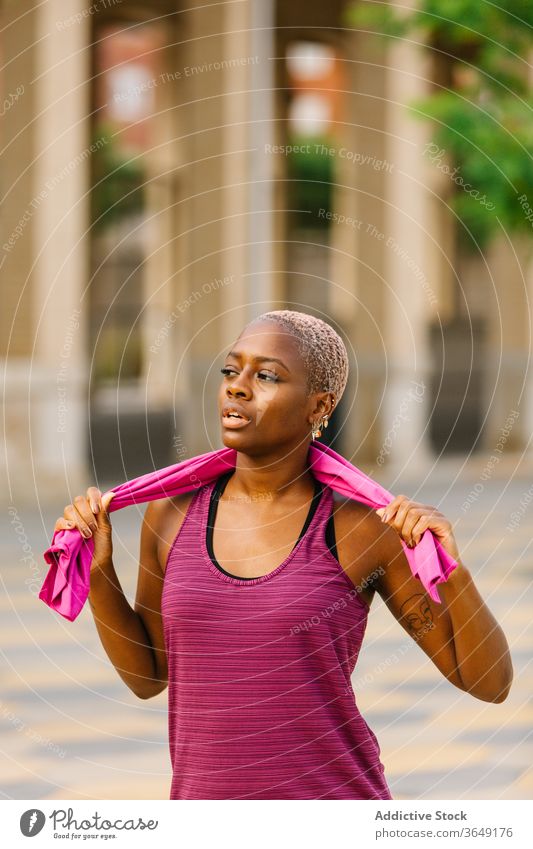 Tired black sportswoman with towel standing on embankment after workout break activewear mouth opened tired healthy building pavement city relax wellness fit