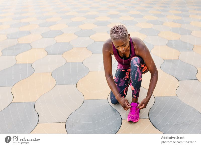 African American athlete tying shoelaces on sneakers during workout sportswoman tie city squat break pavement sportswear colorful urban slender relax thoughtful