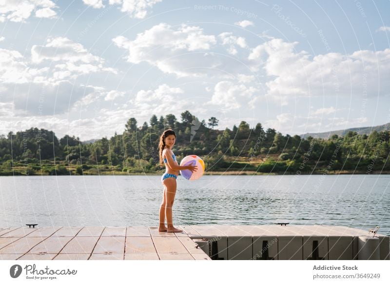 Playful little girl standing in pier near lake beach ball play pond summer holiday vacation enjoy inflatable rubber child bikini water relax kid nature playful