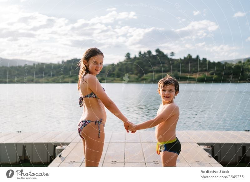 Siblings on wooden pier holding hands lake children summer vacation sibling together swimwear quay brother sister unity friendly friendship happy water smile