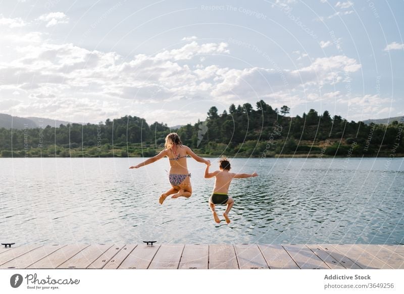 Delighted siblings jumping in lake from pier children having fun water group moment pond childhood swimwear quay wooden weekend summer vacation kid relax joy