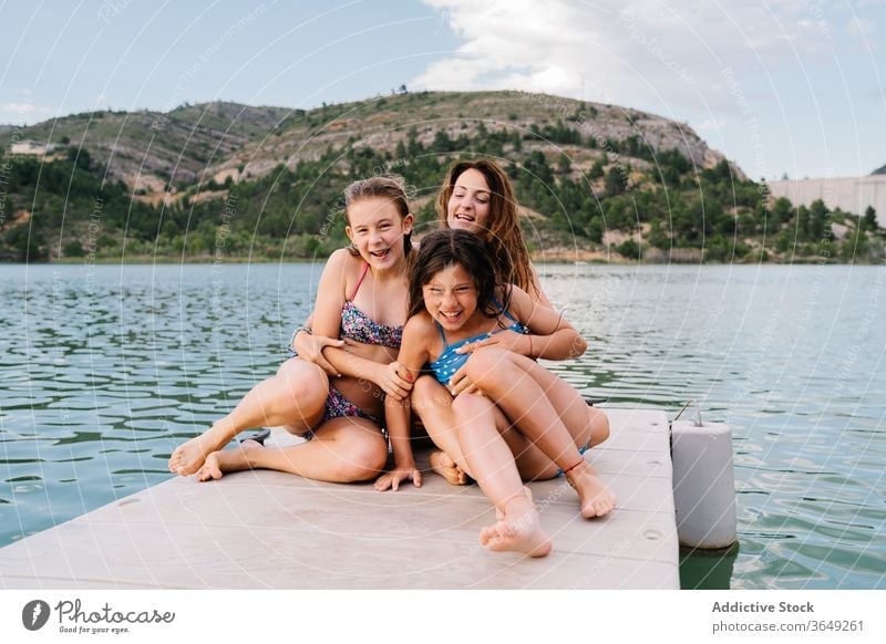 Happy siblings and mother sitting on quay children vacation summer pier relax swimwear content rest happy embrace together unity holiday recreation weekend