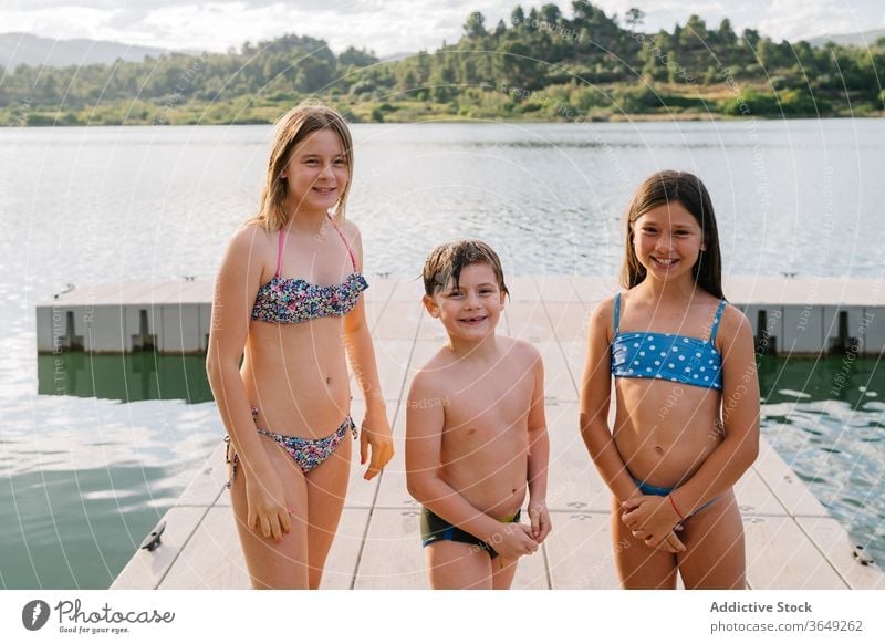 Group of cheerful siblings on wooden pier lake children summer vacation together group swimwear quay brother sister unity friendly friendship happy water rest