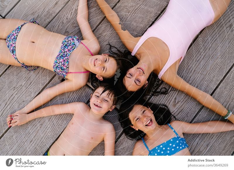 Happy siblings and mother lying on quay children vacation summer pier relax star shape swimwear content rest happy holding hands together unity holiday