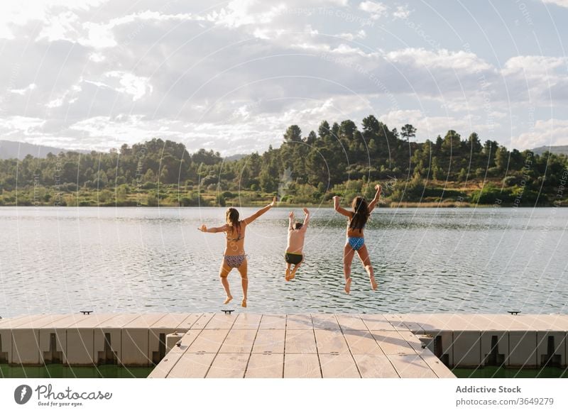 Delighted siblings jumping in lake from pier children having fun water group moment pond childhood swimwear quay wooden weekend summer vacation kid relax joy