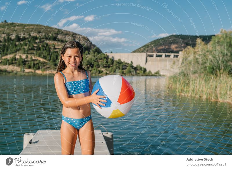 Playful girl standing in pier near lake beach ball play pond summer holiday vacation enjoy inflatable rubber child bikini water relax kid nature playful
