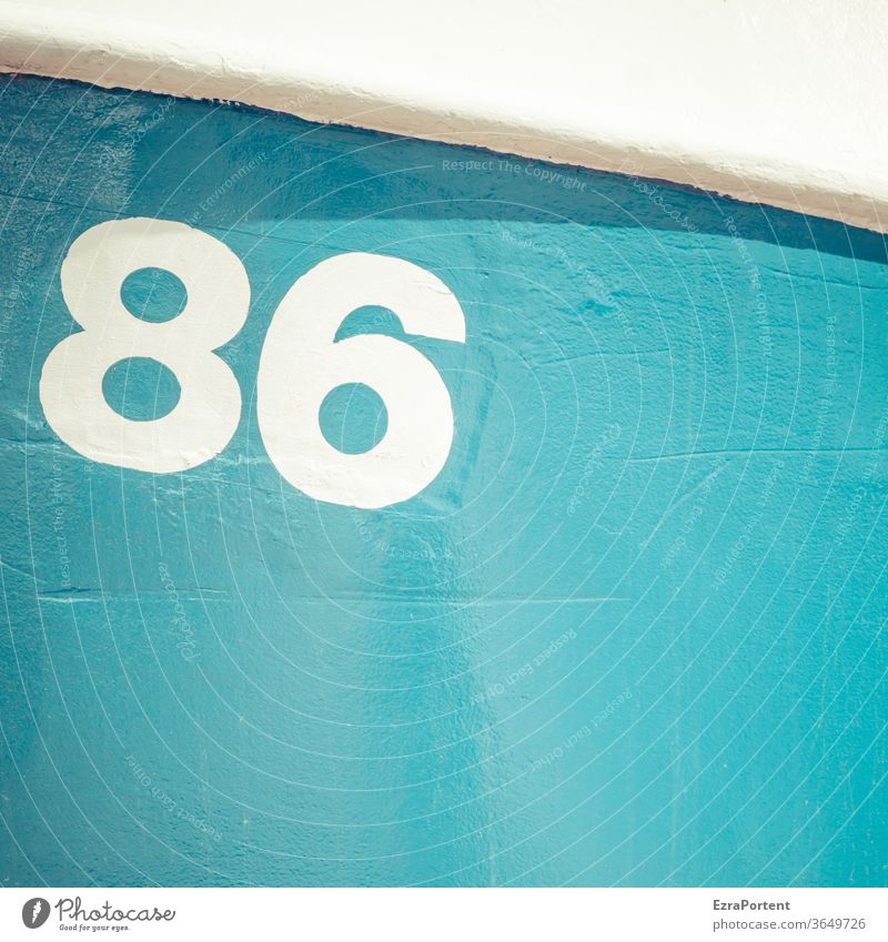 the number 86 on a sunlit blue surface with a white sweep in the upper part casting a bold shadow Blue White Digits and numbers Sign Signs and labeling kind