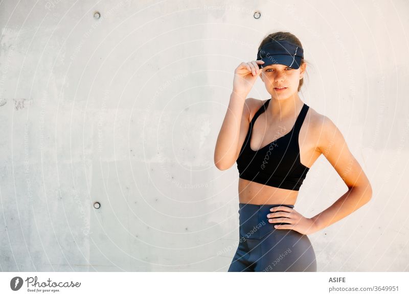 Portrait of a young stylish and beautiful sporty woman model fashion portrait posing running isolated happy smiling runner wall visor cap athlete gorgeous