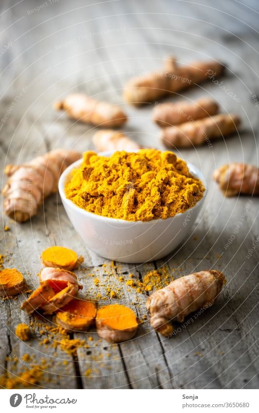 Turmeric roots and powder in a white bowl on a grey wooden table. Close up. Spice. turmeric Root Yellow Powder Organic natural Healthy Close-up cake