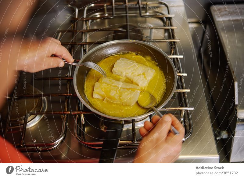 Faceless cook stewing fish fillets in butter in kitchen chef oil process culinary pan stove gas prepare olive melt frying food recipe fork spoon ingredient