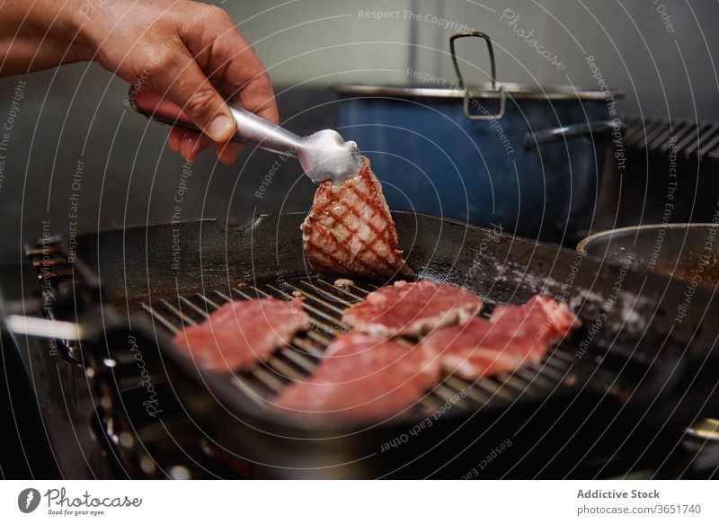 Crop anonymous cook roasting beef fillets on grill pan chef culinary process menu prepare food recipe ingredient dinner lunch organic pot metal tweezers kitchen