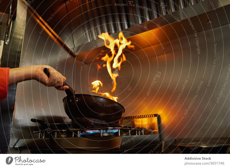 Anonymous chef flambeing food in frying pan on gas stove cook process fire hand restaurant culinary body part prepare ingredient dinner lunch kitchen glassware