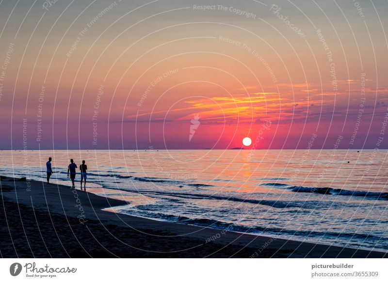 Three people watching the sunrise Sunrise Dawn Sunset Beach Ocean three persons Sky Clouds Horizon Colour photo Summer Waves Water Red Observe Warmth start End