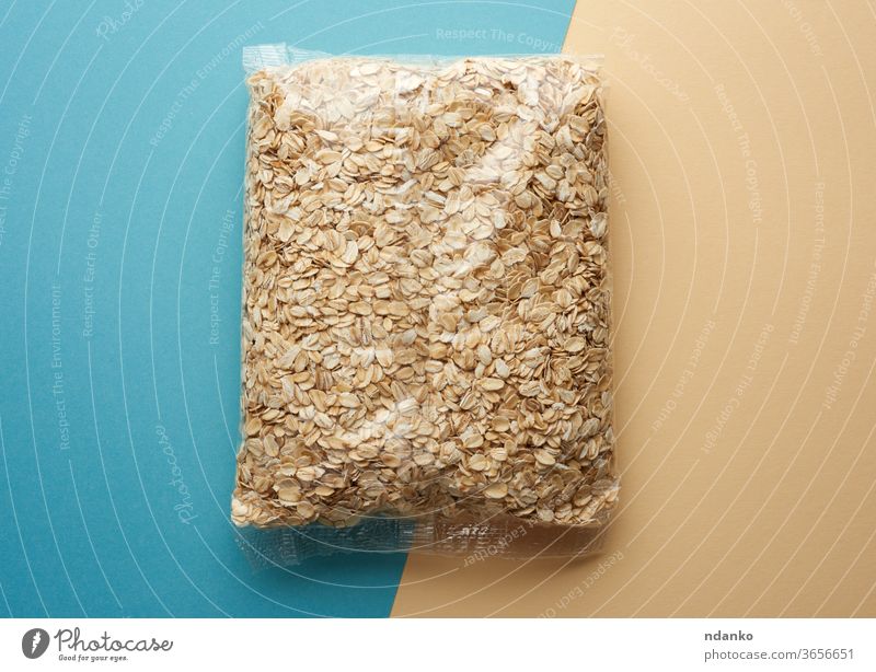 oatmeal in transparent plastic packaging on a blue-beige background organic pile raw seed grocery polyethylene agriculture backdrop breakfast brown cereal