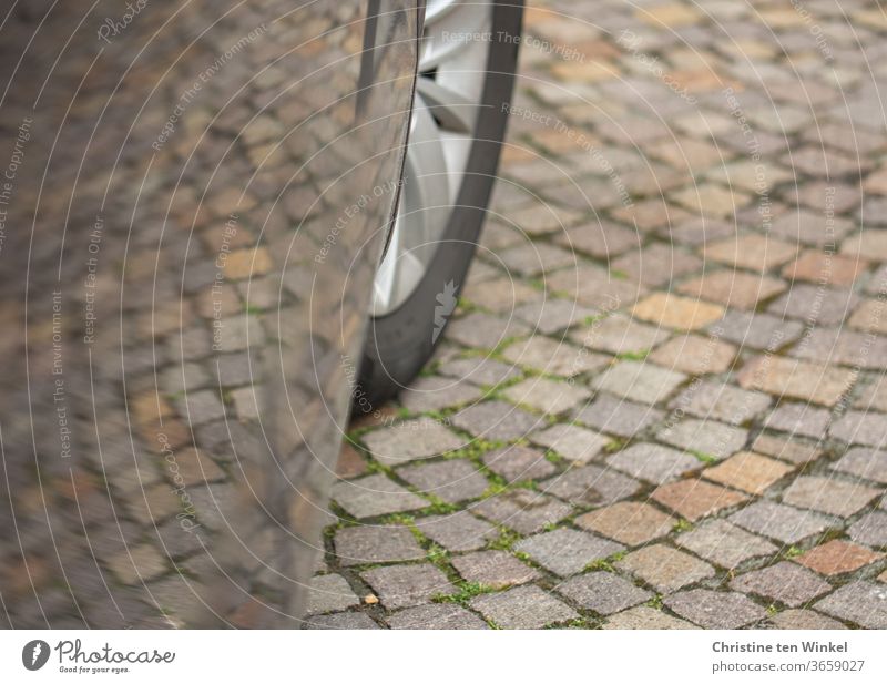 Cobblestone pavement with reflection in the paint of a car door. You can also see a part of the front wheel Car door Reflection Car paint Cobblestones