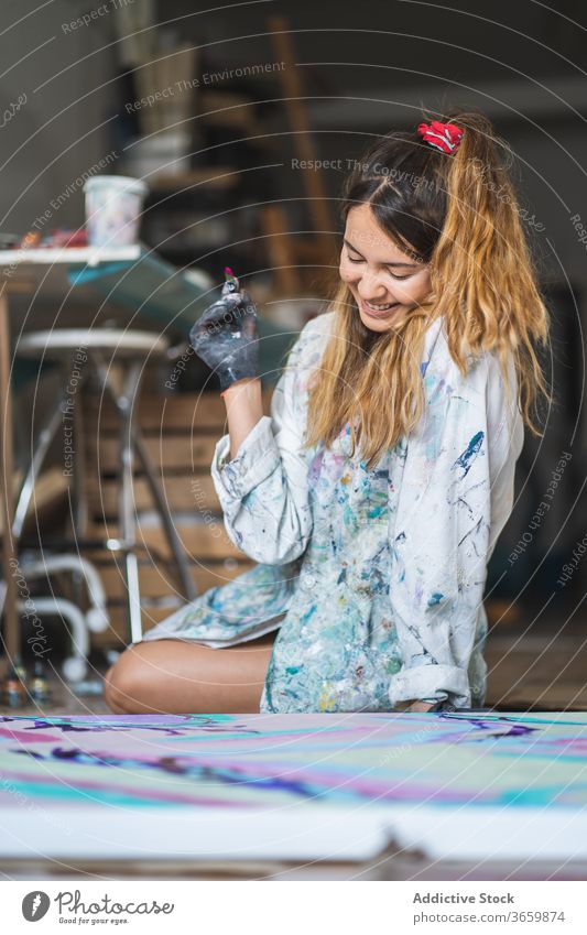 Happy female painter laughing while looking at colorful picture art craft talent liquid barefoot glove workshop artist paper multicolored content studio hobby