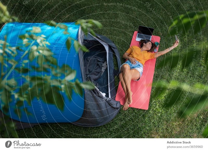 Happy woman taking selfie near camping tent smartphone happy summer rest enjoy gadget cheerful smile mobile lying modern nature relax meadow grass young female