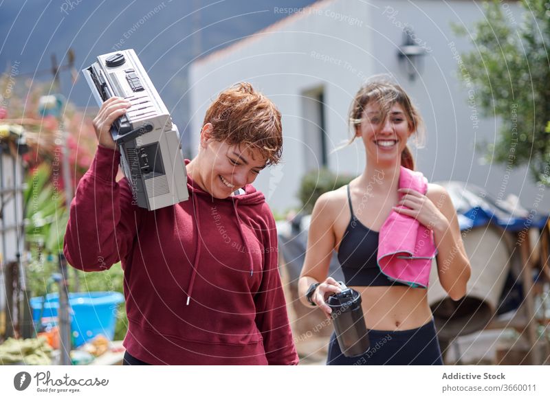 Excited sportswomen with boombox walking in backyard rest country happy excited listen fitness sportswear relax workout together athlete joy strong toothy smile