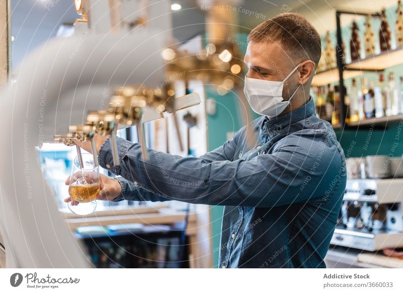 Young man filling glass with beer for client pour tap fresh bartender mask pub draught alcohol drink work male young shirt positive coronavirus covid beverage