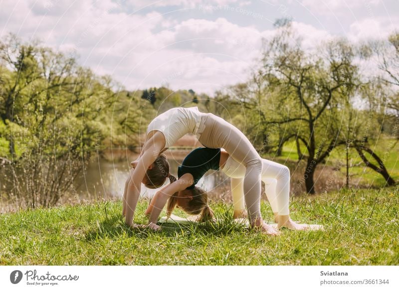 Young mother and daughter doing yoga in the open air in the Park. A girl and her daughter perform exercises together. The concept of family child health asana