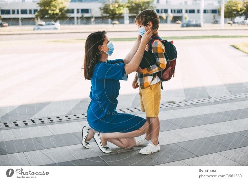 Mom puts a child a mask and escorts to school or kindergarten. A boy with a masked backpack during a coronavirus. Side view mother back to school face