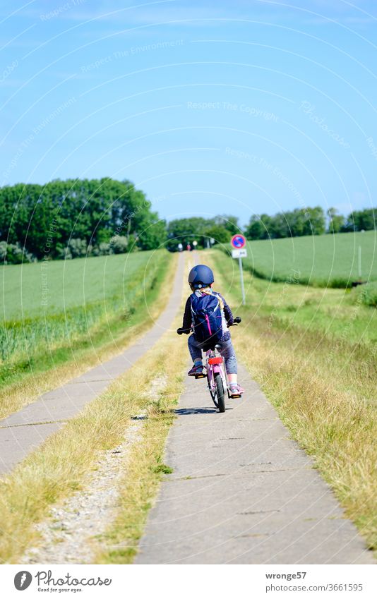 Northwards | child cycles on a flat path towards the cliffs Child girl paved path arable track off the beaten track steep coast Exterior shot Colour photo Field