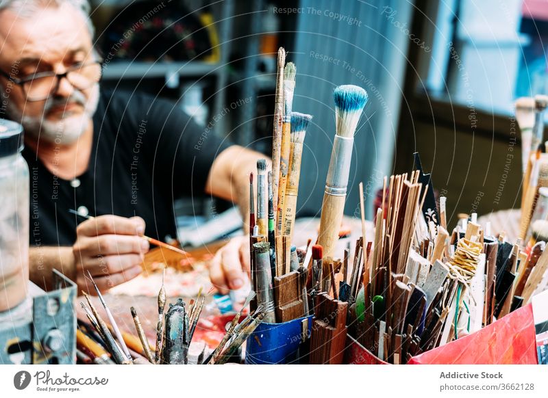 Male artist working behind set of various paintbrushes designer workplace studio collection small business sketch focus occupation profession watercolor painter