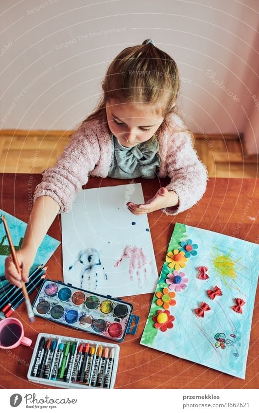 Little girl in preschool age, who paints a picture with bright colours and crayons. Child who has fun painting a picture during an art lesson in the classroom