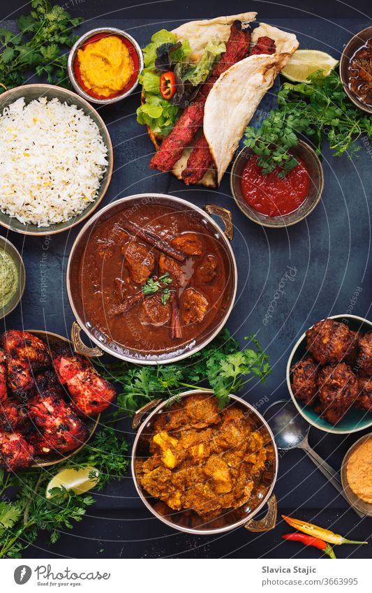 Various Indian dishes featuring  rogan josh, chicken tikka masala,tandoori chicken wings  and  kebabs, with rice and naan bread above appetizer asian assorted