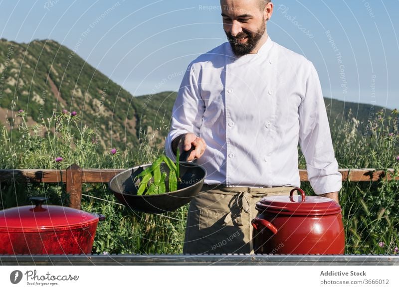 Professional chef cooking in countryside on sunny day man dish spice pan nature workshop prepare happy professional beard tunic uniform cheerful joy job glad