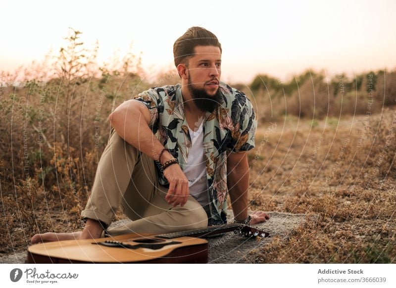 Cheerful barefoot guitarist with guitar in field musician cheerful hipster rug grass sky harmony man musical instrument play idyllic countryside sit acoustic