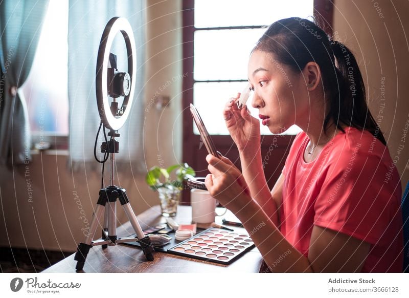 Beauty blogger applying makeup during shooting session beauty vlog woman cosmetic foundation record video young asian female ethnic camera light lamp mirror