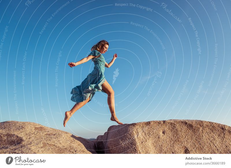 Active young lady running on huge stones during sunset woman jump rocky cliff happy style recreation freedom summer blue sky holiday cheerful female slim dress